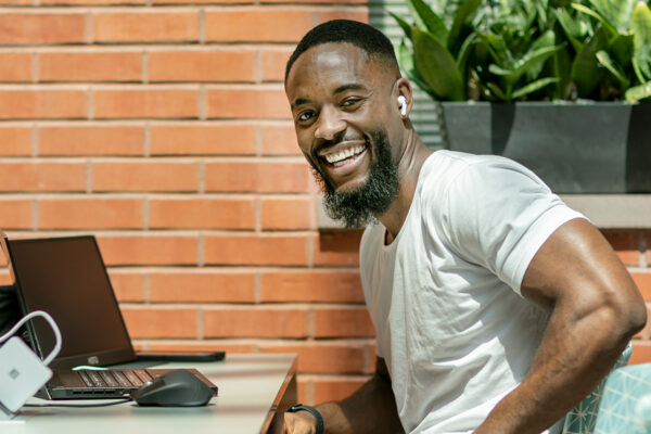 A student in a white t-shirt sits in front of two laptops and smiles.